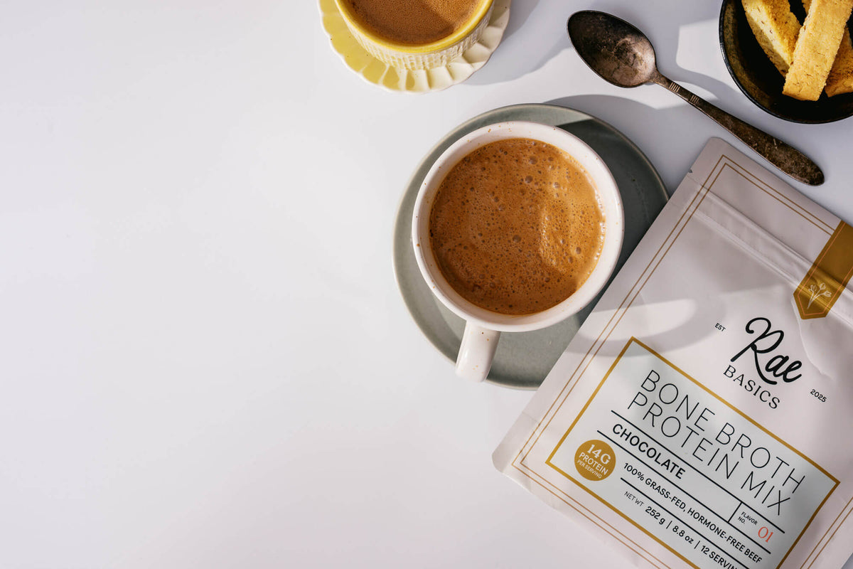 Overhead view of a frothy mug of protein coffee beside a bag of Classic Chocolate Bone Broth Protein Mix