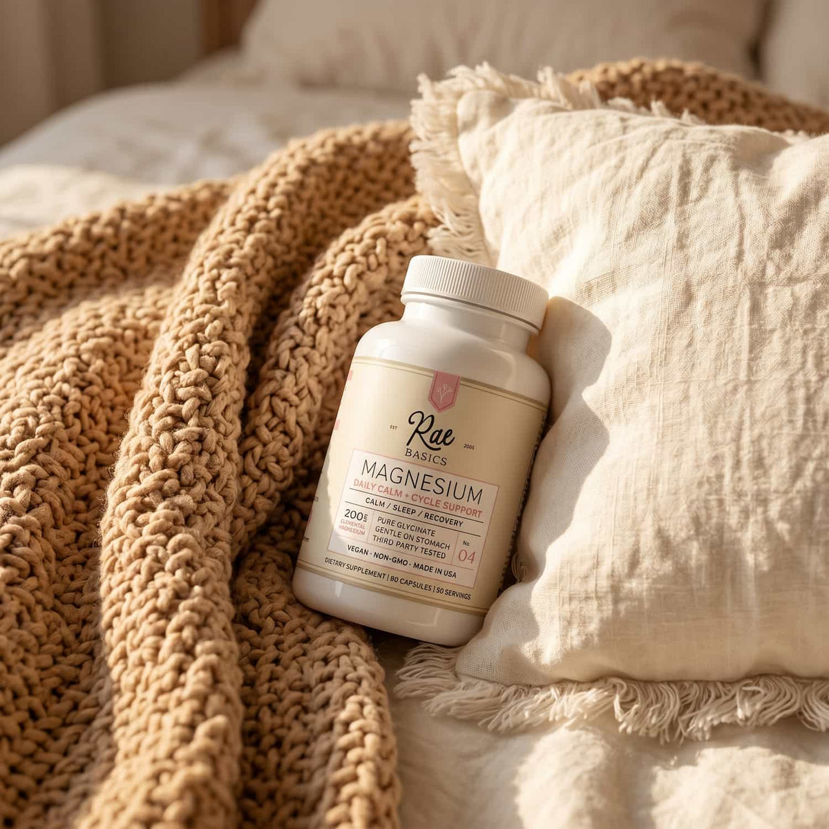 Bottle of Rae Basics NO. 04 Magnesium Glycinate resting on a knit blanket and linen pillow