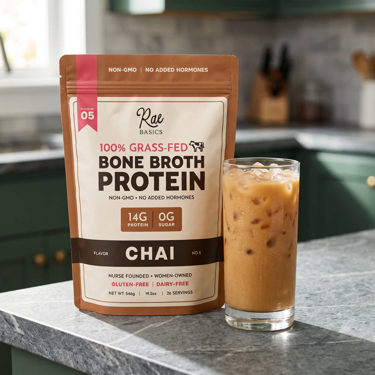 Bag of Rae Basics Chai Bone Broth Protein Mix beside a glass of iced chai on a kitchen counter