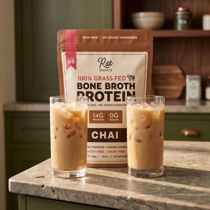 Two glasses of iced chai latte in front of a bag of Rae Basics Chai Bone Broth Protein Mix on a kitchen counter